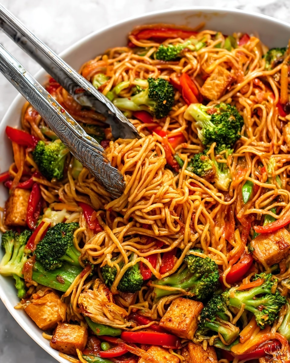 The image shows a pan of stir-fried noodles with several layers and colors. At the bottom are curly yellow noodles spread evenly. On top are many pieces of cooked chicken, light brown with a slightly crispy texture, placed in different spots around the pan. Mixed in and around the chicken are thin strips of red bell pepper, soft green lettuce leaves, and some small slices of light green cucumber. A woman's hand is holding wooden chopsticks picking up some noodles and chicken from the right side of the pan. The pan is placed on a white marbled surface. photo taken with an iphone --ar 4:5 --v 7
