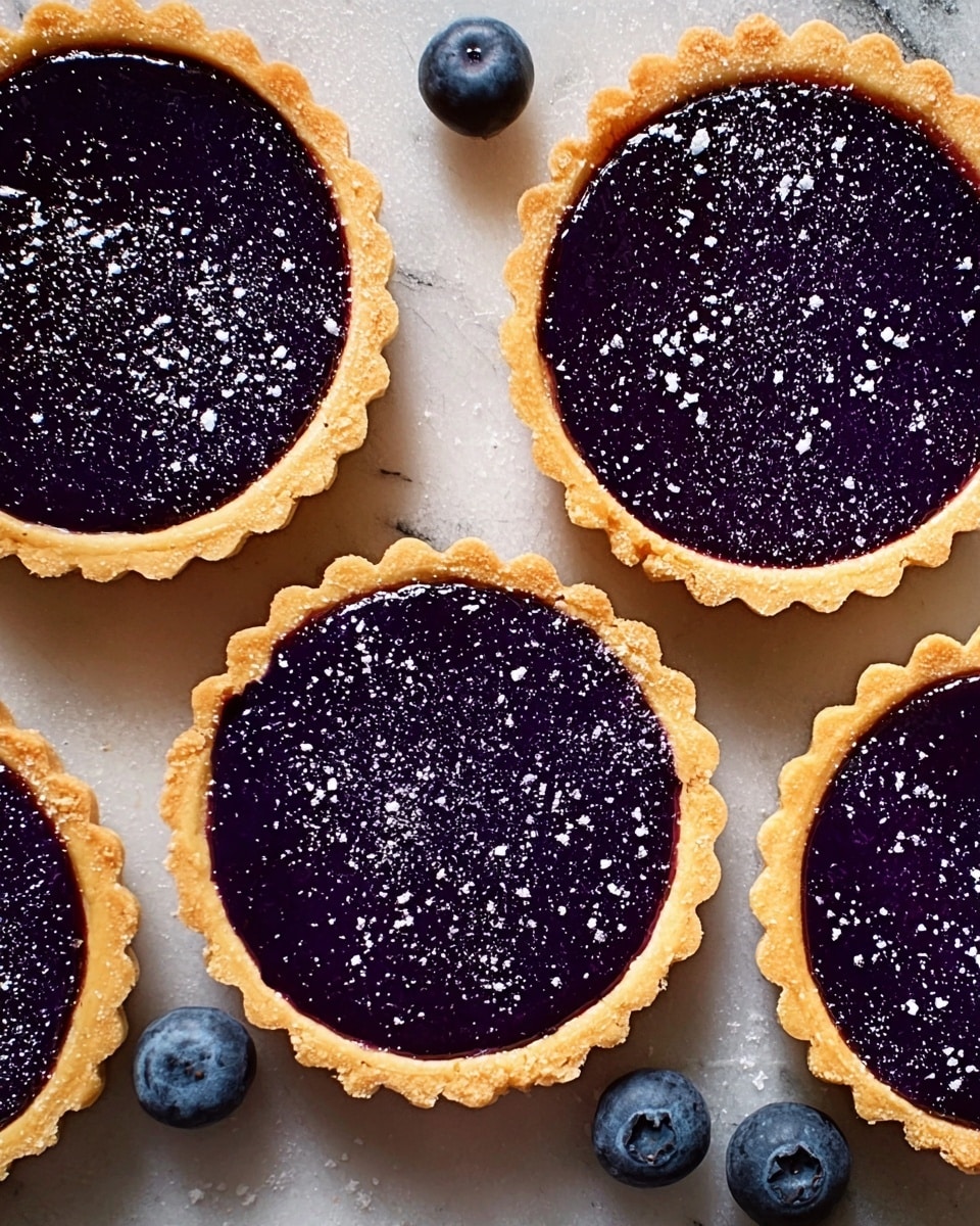 Five small tarts are shown from above on a white marbled texture. Each tart has a golden-brown, crisp, and wavy-edged crust forming the base and sides. Inside each crust is a smooth, shiny, deep purple filling that fills the tart completely and looks glossy. There are small white specks lightly sprinkled on top of the filling, resembling powdered sugar, creating a delicate contrast. Two fresh blueberries with a deep blue color and a natural texture rest nearby on the white marbled surface. The tarts are arranged close together, showing their round shapes clearly. photo taken with an iphone --ar 4:5 --v 7