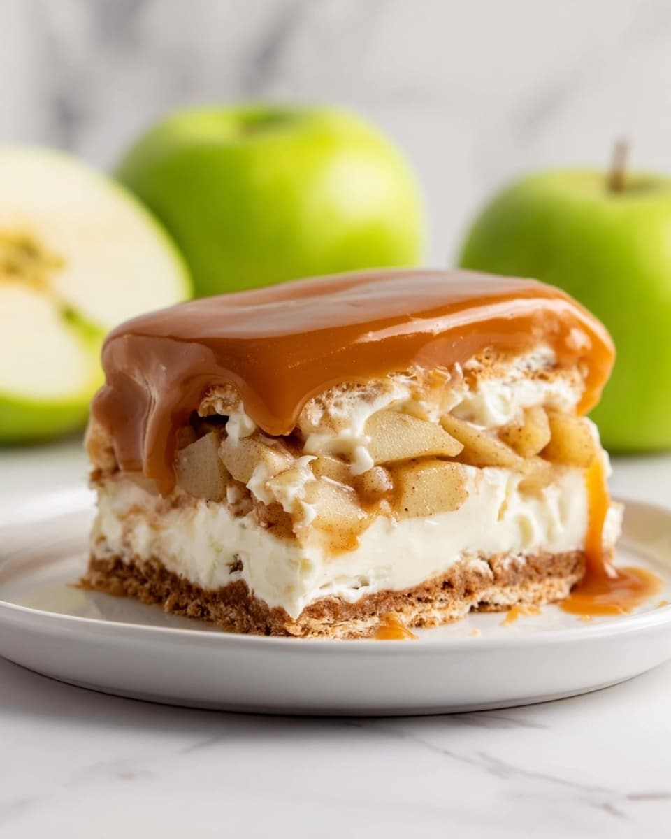 A layered dessert with three visible layers sits on a white plate against a white marbled texture. The bottom layer is a light brown biscuit or crust base. The middle layer consists of creamy white filling mixed with soft chunks of cooked apple, with some cinnamon or spice visible in the mix. The top layer is a thick, smooth caramel glaze that has a shiny, rich brown color, slightly draping down the sides. Two green apples, one whole and one cut in half, are out of focus in the background. The photo taken with an iphone --ar 4:5 --v 7
