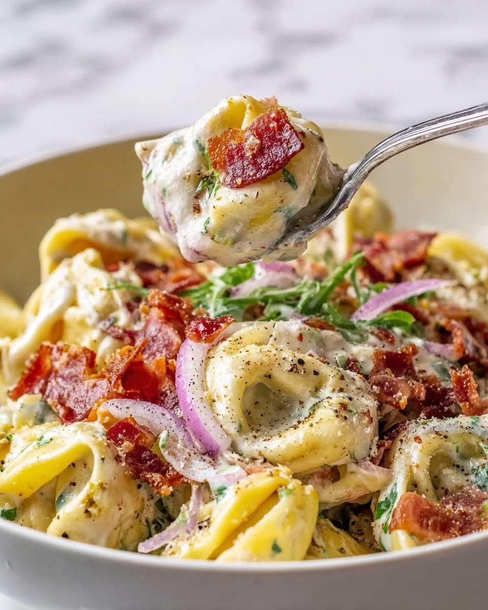 The dish shows a close-up of creamy tortellini pasta with three main layers: the tortellini with a pale yellow color and soft texture forms the base, topped with a generous layer of white creamy sauce with green herbs mixed in, and scattered crispy red bacon pieces on top, along with some flecks of black pepper and grated white cheese. Thin slices of purple onion and small green leaves peek through among the pasta. A silver fork lifts a tortellini piece covered in sauce and bacon above the dish. The bowl holding the food is white, placed on a white marbled texture surface. Photo taken with an iphone --ar 4:5 --v 7